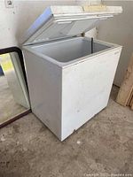 White chest freezer with top lid open, showing exterior scuff marks and dirt.