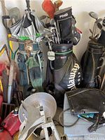 Photo showing three golf bags filled with various golf clubs including Callaway and PING brands, alongside other items in a garage.
