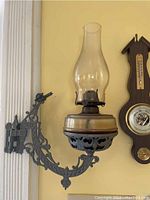 Front view of antique hanging oil lamp mounted on ornate wood and metal bracket with glass chimney and copper burner.