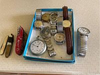Overview of box containing assorted wristwatches, Waltham pocket watch and two folding knives