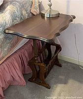 Full view of walnut side table showing scalloped tabletop and lamp on top.