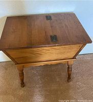 Front angle showing small maple side table with hinged lid closed and turned spindle legs.