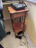 Full view of cherry wood side table showing top and carved spindle supports, with cables and electronic device on top