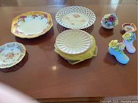 Full view of various china plates and porcelain figurines arranged on a wooden table.