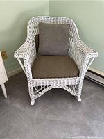Front view of antique white wicker rocking chair with green cushions, showcasing woven wicker pattern and front legs.