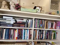 Wide view of a white bookshelf with three shelves filled with various books of different colors and sizes.