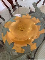 Top and angled view of large gold centerpiece bowl with etched leaf motifs around rim, placed on a glass table.