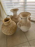 Front view of two fluted-top ceramic vases and one etched round ceramic pot on tiled floor near window blinds.