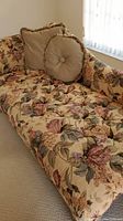 Image of floral tan chaise lounge with deep rose floral pattern, including two pillows with fringed edges.