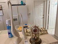 Two white bird statues displayed on kitchen counter with a can of spray nearby. Taller bird statue shows repair evidence on neck and base. Quartz table clock with glass dome partially visible on right side.