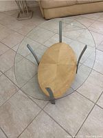 Top view of coffee table showing clear beveled oval glass surface and wooden base supported by metal legs.