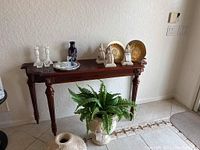 Full view of the console table positioned against a wall, with various decorative items displayed on top and a potted fern underneath