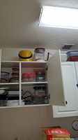 Open kitchen cabinet shelves showing mixed plastic containers with lids in various sizes and colors