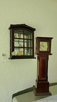 View of wall-mounted curio cabinet and tall wooden clock side by side