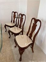 Seven dark wood dining chairs lined up, beige seats mostly covered with plastic.