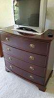 Front view of the wood four drawer dresser with a TV on top.