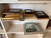 Shelf with multiple frames stacked and arranged showing various styles and materials.