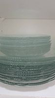 Stack of clear textured glass plates and bowls on white shelf.