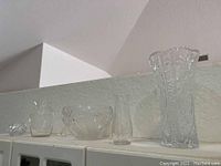Wide view of the five glass items grouped in a line on a shelf, showing varying sizes and shapes under ambient indoor lighting.