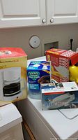 Photo showing the boxed and unboxed items including the Vicks steam inhaler, Sunbeam coffee pot, travel steam iron, and part of the hair dryer in a red and white box.