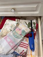 Drawer showing kitchen towels with floral and scenic prints along with a blue utility lighter.