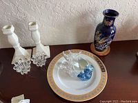 Overview of all items: porcelain plate, white and clear candle holders, blue decorative vase, and three figurines on a shelf