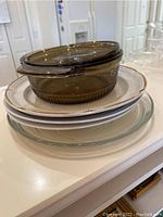 Stack of four plates with a glass lidded casserole dish on top, showing the casserole and the top plate clearly