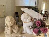 Angel statue with pink rose flowers and wings, showing off-white ceramic with some staining.