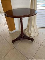 Front and side view of the round wooden pedestal table showing carved center leg and tripod base.