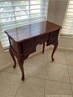 Full view of the wood entrance desk table showing its curved edges, three drawers, and cabriole legs.