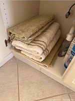 Bath rugs folded and stacked on an open cabinet shelf, alongside bathroom items