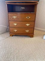 Front view of wood TV cabinet showing swivel top, three drawers with brass handles, and open shelf space.