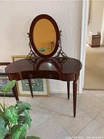 Front view showing the kidney-shaped wood vanity table with oval mirror and brass candle holders on each side.