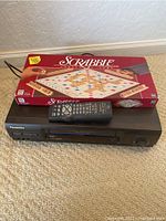 Panasonic VCR with remote control and Scrabble board game box placed on floor