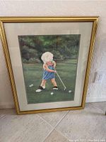 Full view of the framed wall art showing the child golfer image, gold frame, and matting.