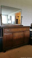Front view of wooden buffet with brass hardware and large ornate mirror above it. Shows multiple drawers and cupboard doors on the buffet.