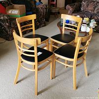 Four wooden chairs with black leather seats arranged in a circle.