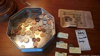 Metal tin containing assorted US coins with a German 100,000 Mark banknote and several labeled envelopes laid on wood surface.
