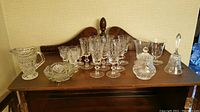 Full set of crystal glassware including glasses, sugar bowl, milk cup, candy bowl, pitcher and bell on wooden surface