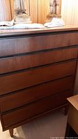 Frontal view of a five drawer wooden dresser showcasing horizontal inset handles and a medium brown finish with minor scratches.