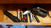 Photo showing seven flashlights, one silver multi-tool, one red-handled manicure set, and a folded black umbrella in a drawer.