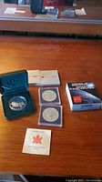 Lot includes three Canadian silver dollar coins from 2000. One coin is a proof coin housed in a green velvet-lined display case with accompanying boxes and booklet.