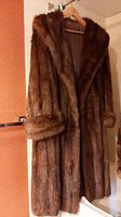 Full-length view of the muskrat fur coat hanging on a hanger against a wall.