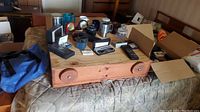 Full view of collection on wooden box and bed showing diverse Nortel branded swag items including clocks, cups, a blue bag, various small box packaging, and a remote control.