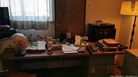 Wide angle photo showing the entire desk with a variety of office supplies including a globe, briefcases, papers, writing tools, and desk accessories.