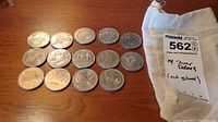 14 Canadian silver dollar coins spread on a surface next to a fabric pouch labeled with handwritten details.