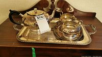 Full set on tray showing teapot, sugar bowl, and milk cup placed on an engraved silver tray.