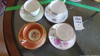 Four assorted vintage tea cups and saucers on table showing different floral patterns and styles with gold trimming.