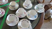 Set of seven floral tea cups and saucers arranged on glass tabletop plus two additional saucers