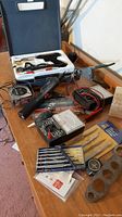 Photo showing Weller glue gun in styrofoam case, wire cutter, tape measure, Ohm meter, screwdriver set, and wrenches on wood surface.